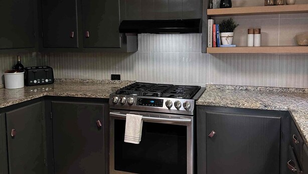 A kitchen with dark cabinets, a stainless steel stove, and a tiled backsplash.
