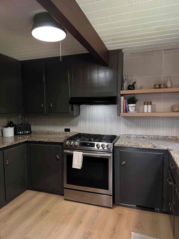 A kitchen with dark cabinets, a stainless steel stove, and a tiled backsplash.