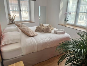 Ein Schlafzimmer mit Bett, Kissen, einem Nachttisch, einem Spiegel und einem Fenster mit Blick.