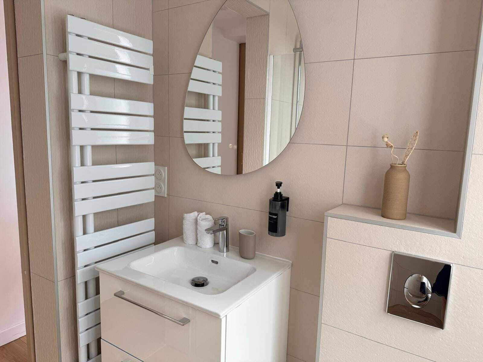 A modern bathroom with a white vanity, a round mirror, and a towel rack.