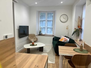Ein modernes Wohnzimmer mit einem Holzesstisch, einem grünen Sofa, einem weißen Couchtisch und einer Wanduhr.