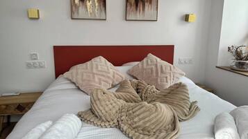 Ein ordentlich bezogenes Bett mit rotem Kopfteil, zwei an der Wand montierte Lichtschalter und zwei abstrakte Gemälde darüber.