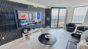 Ein modernes Wohnzimmer mit Fernseher, einer Couch, einem Couchtisch und einem Balkon mit Blick.