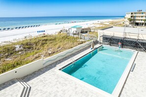 Ein Pool mit Blick auf den Strand, ein Rettungsturm und ein Gebäude mit Balkon.