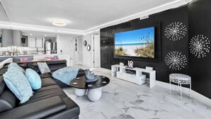 Un salon moderne aux couleurs noir et blanc, doté d’un grand téléviseur à écran plat et agrémenté d’œuvres d’art décoratives sur les murs.