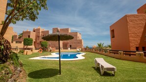 A swimming pool surrounded by grass, with a lifebuoy and a thatched umbrella nearby. - Coto Real apartment Zira 321 (Manilva)