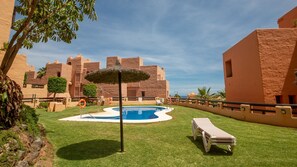 A swimming pool surrounded by grass, with a lifebuoy and a thatched umbrella nearby. - Coto Real apartment Zira 321 (Manilva)