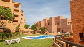 A pool area with a clear blue pool, surrounded by a low fence, and adjacent to a building with a flat roof and multiple windows. - Coto Real apartment Zira 321 (Manilva)