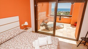A hotel room with a bed, a nightstand, a lamp, and a view of a balcony with a table and chairs. - Coto Real apartment Zira 321 (Manilva)