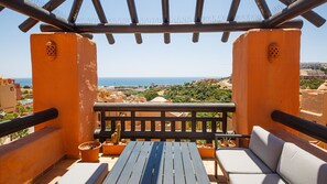 Une terrasse avec une table en bois et deux canapés, donnant sur une ville côtière.