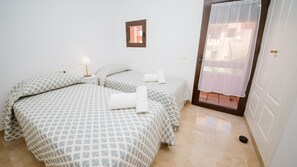 Une chambre d’hôtel avec deux lits, une petite fenêtre et une porte donnant sur un balcon.