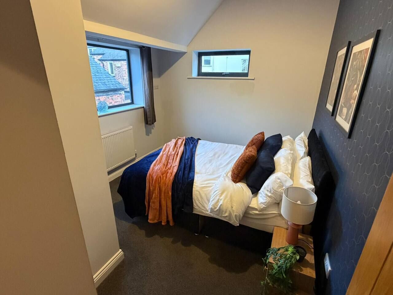 Une chambre à coucher avec un lit, une fenêtre, une petite lucarne et une étagère fixée au mur.