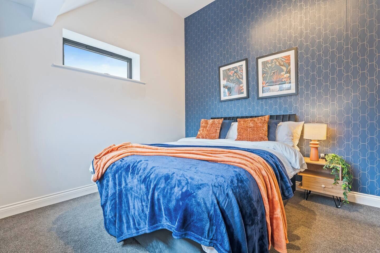A bedroom with a bed, a nightstand, a lamp, and two framed pictures on the wall.