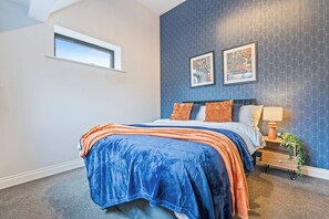A bedroom with a bed, a nightstand, a lamp, and two framed pictures on the wall. - #125 Cozy Retreat Near LeicesterCathedral|Sleeps 8 (Leicester)