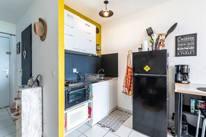 A compact kitchen with a stove, oven, and refrigerator, featuring a yellow accent wall and a blackboard with French phrases. - Le Cocon de Moriani - Climatisé et plage à 100 m (San-Nicolao)