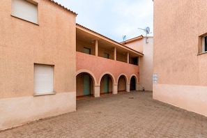 A courtyard with a building featuring a balcony with arches, a satellite dish, and a sign on the wall. - Le Cocon de Moriani - Climatisé et plage à 100 m (San-Nicolao)