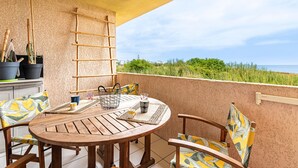 Un tavolo di legno con sedie, una scala e piante in vaso su un balcone con vista su vegetazione ed edifici.