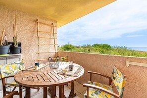 Ein Holztisch mit Stühlen, eine Leiter und Kübelpflanzen auf einem Balkon mit Blick auf Grünflächen und Gebäude.