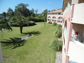 A building with a covered outdoor area, a lawn, and palm trees. - Le Cocon de Moriani - Climatisé et plage à 100 m (San-Nicolao)