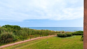 Paesaggio costiero con una passeggiata lastricata, vegetazione e vista sul mare.