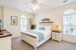 Une chambre à coucher comprenant un lit, des tables de chevet, un bureau et un ventilateur de plafond.