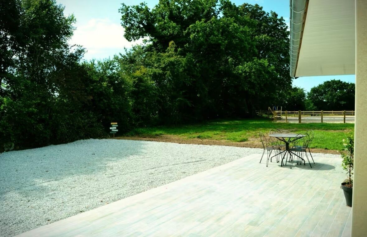 A patio area with a gravel surface, a round table with chairs, and a potted plant.