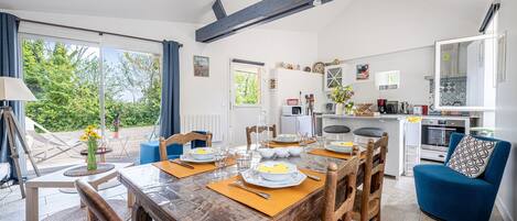 A modern kitchen with a dining area, a blue sofa, and a view of greenery outside.