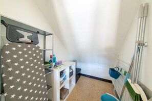 A laundry room with a drying rack, ironing board, shelves with folded clothes, and cleaning supplies.