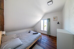 A bedroom with a single bed, a radiator, a window with curtains, and a framed picture on the wall.