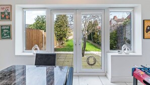 Um quarto com uma mesa de jantar, duas janelas com vista para um jardim e uma mesa de pebolim.