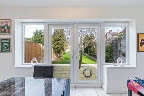 A room with a dining table, two windows with a view of a garden, and a foosball table. - #126 Cosy 5 mins to Coventry Cathedral | sleeps 7 (West Midlands)