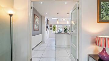 A hallway with a kitchen area, white tiled flooring, and pendant lighting.