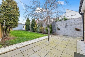 A residential backyard with a lawn, a small tree, a white brick wall, and a shed. - #126 Cosy 5 mins to Coventry Cathedral | sleeps 7 (West Midlands)