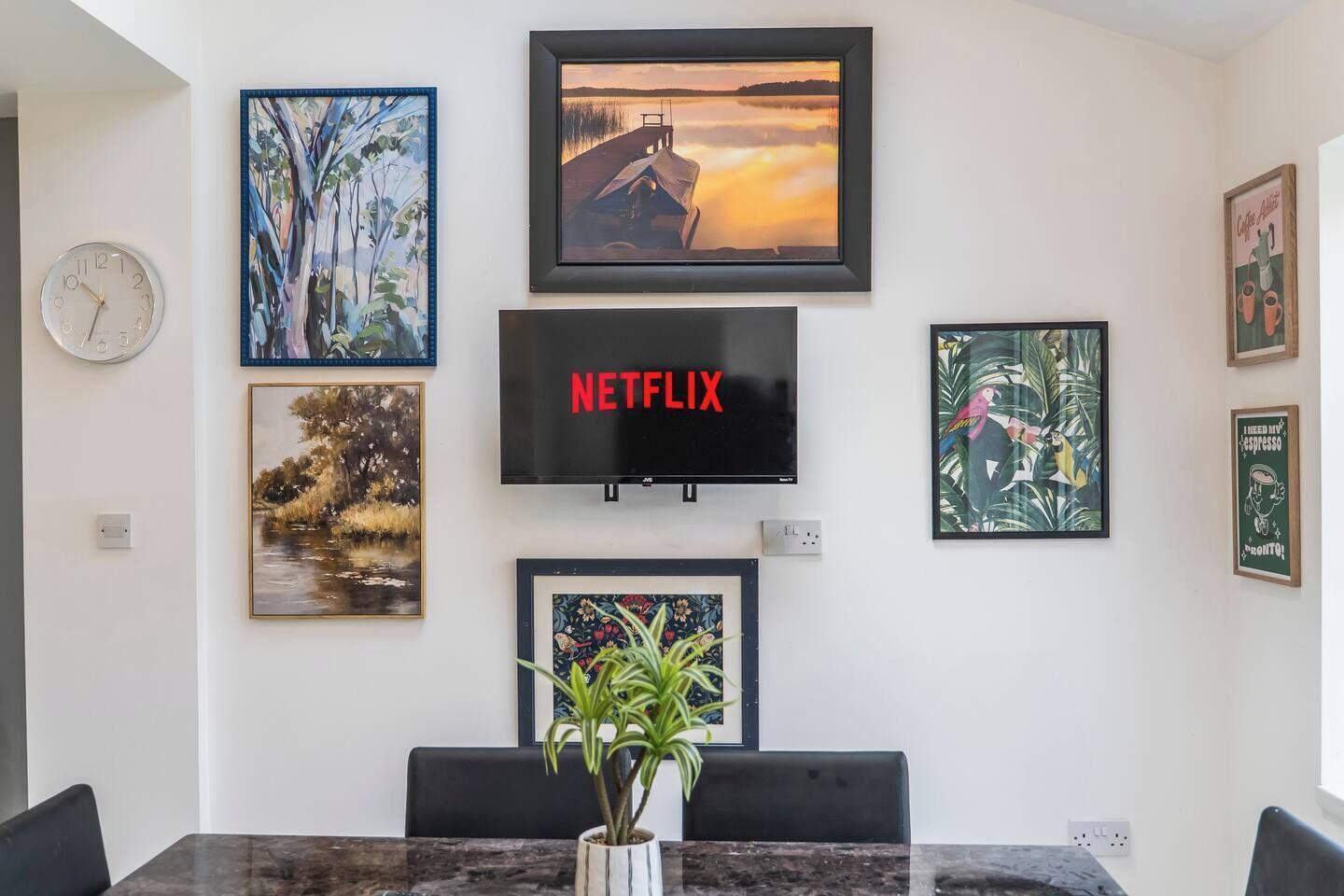 Um quarto com uma TV fixada na parede, um relógio e várias obras de arte emolduradas.