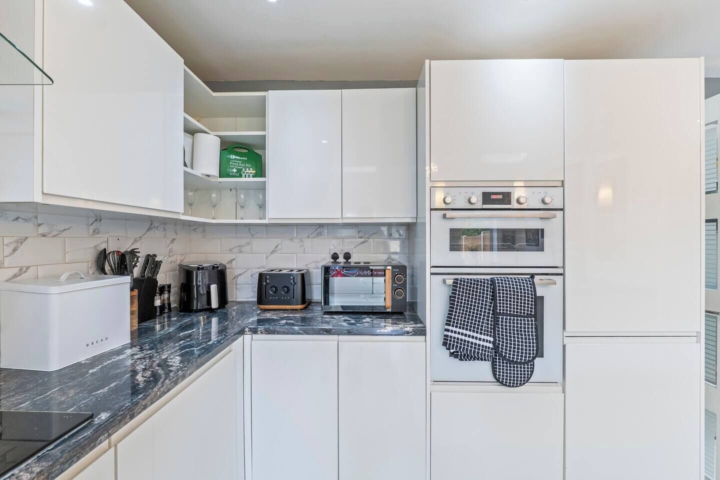A modern kitchen with white cabinets, a built-in oven, a toaster, and a coffee maker.