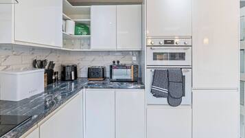 A modern kitchen with white cabinets, a built-in oven, a toaster, and a coffee maker.