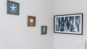 Um corredor com três obras de arte emolduradas na parede, uma escada com corrimão branco e uma parede branca lisa.