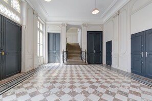 Eine prachtvolle Eingangshalle mit Schachbrettfußboden, doppelten Türen und einer Treppe, die in eine obere Ebene führt.