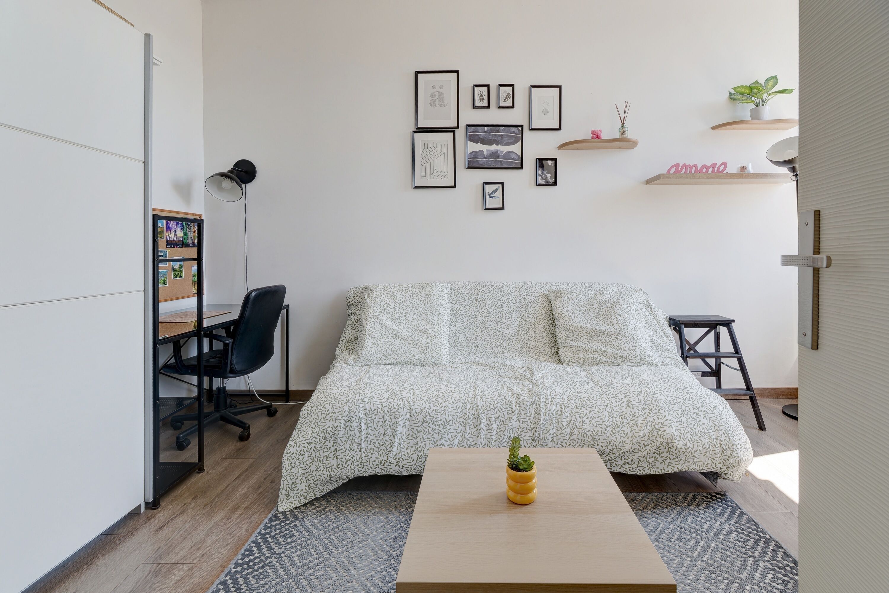 A modern bedroom with a bed, a desk, a chair, and a small table with a plant.