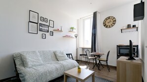A modern living room with a sofa, a small table, a TV, and a dining area with chairs and a table. - L'Escale Rémoise - À 600 m de la Porte de Mars (Reims)