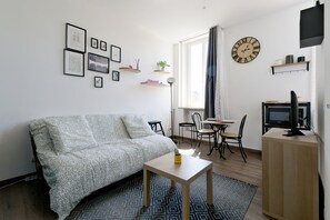 A modern living room with a sofa, a small table, a TV, and a dining area with chairs and a table. - L'Escale Rémoise - À 600 m de la Porte de Mars (Reims)