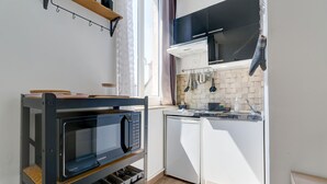 A compact kitchen with a built-in microwave, white cabinets, and a window providing natural light. - L'Escale Rémoise - À 600 m de la Porte de Mars (Reims)