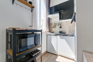 A compact kitchen with a built-in microwave, white cabinets, and a window providing natural light. - L'Escale Rémoise - À 600 m de la Porte de Mars (Reims)