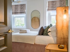 A bedroom with a bed, a bedside table, a mirror, and a window with curtains.