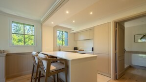 Una cucina moderna con isola centrale, sedie in legno e vista sull'esterno tramite ampie finestre.