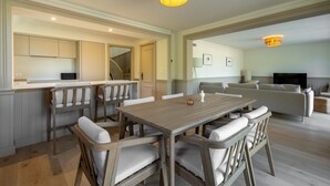 Una zona pranzo con tavolo e sedie in legno, una cucina con pensili e un soggiorno con divano e televisore.