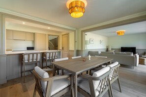 Ein Essbereich mit Holztisch und Stühlen, eine Küche mit Schränken sowie ein Wohnzimmer mit Sofa und Fernseher.