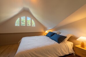 A bedroom with a sloped ceiling, a large bed, two bedside lamps, and a window with a view of trees. - L'Océan du Ferret - Climatisé et plage à 500 m (Lège-Cap-Ferret)