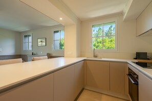 Eine moderne Küche mit einer großen Kochinsel, einem Fenster mit Blick auf Grünflächen und einem eingebauten Backofen.
