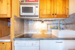 A kitchen with wooden cabinets, a microwave, a dishwasher, and a sink. - Le Repos des Horizons - Proche station de ski (Huez)